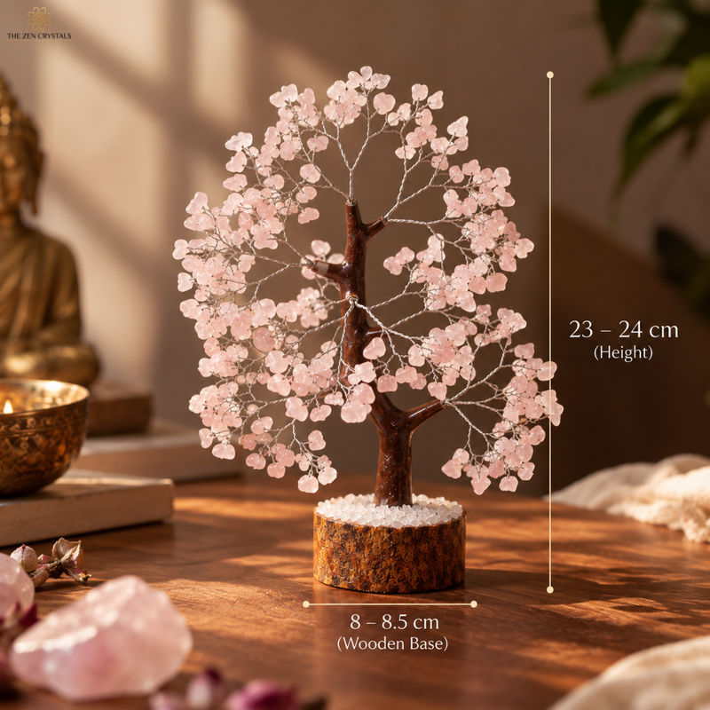 A pink crystal tree of joy with a brown wire trunk and a round wooden base, shown on a wooden table with dimension overlays indicating a height of 23-24 cm and a base width of 8-8.5 cm.