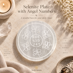 A round translucent selenite crystal plate with engraved angel numbers and symbols, styled on a beige fabric surface with a lit candle, quartz crystal, dried flowers, and a small dish. Text reads 'Selenite Plate with Angel Numbers' and 'The Zen Crystals'.