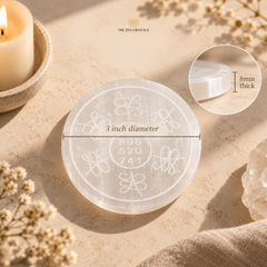 A round translucent white crystal plate with engraved geometric and floral patterns, shown on a warm beige surface with a candle, dried flowers, and a crystal cluster. The image includes a measurement overlay indicating 3 inch diameter and a thickness callout showing 8mm thick.