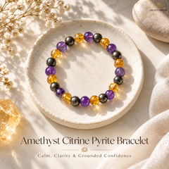 A beaded stretch bracelet displayed on a round ceramic dish, featuring purple amethyst, yellow citrine, and metallic dark gray pyrite beads. The scene is styled with natural elements, linen fabric, and text overlay reading 'Amethyst Citrine Pyrite Bracelet'.
