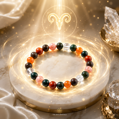 Aries zodiac bracelet displayed on a white marble pedestal with glowing golden light effects. The bracelet features a mix of polished gemstone beads in orange, dark green, red, black, and clear, with a glowing ram symbol and crystals in the background.