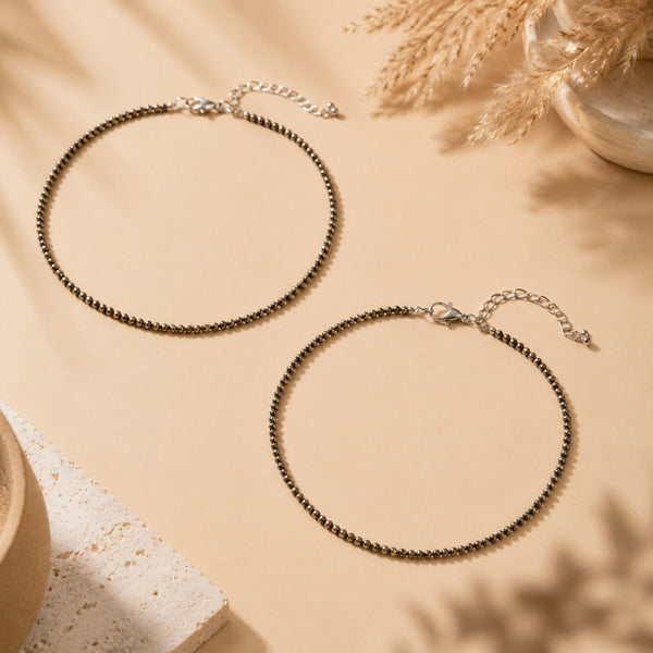 Two pyrite anklets on a beige surface with dried plants and a stone.